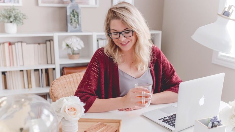woman smiling holding glass mug sitting beside table with MacBook