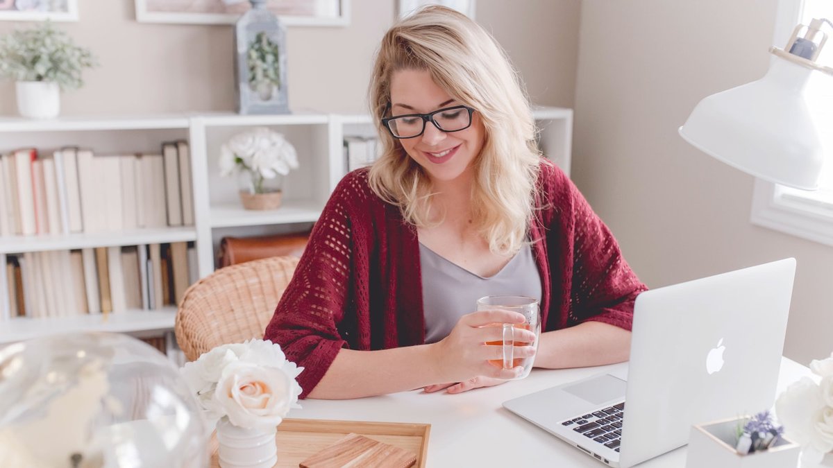 woman smiling holding glass mug sitting beside table with MacBook